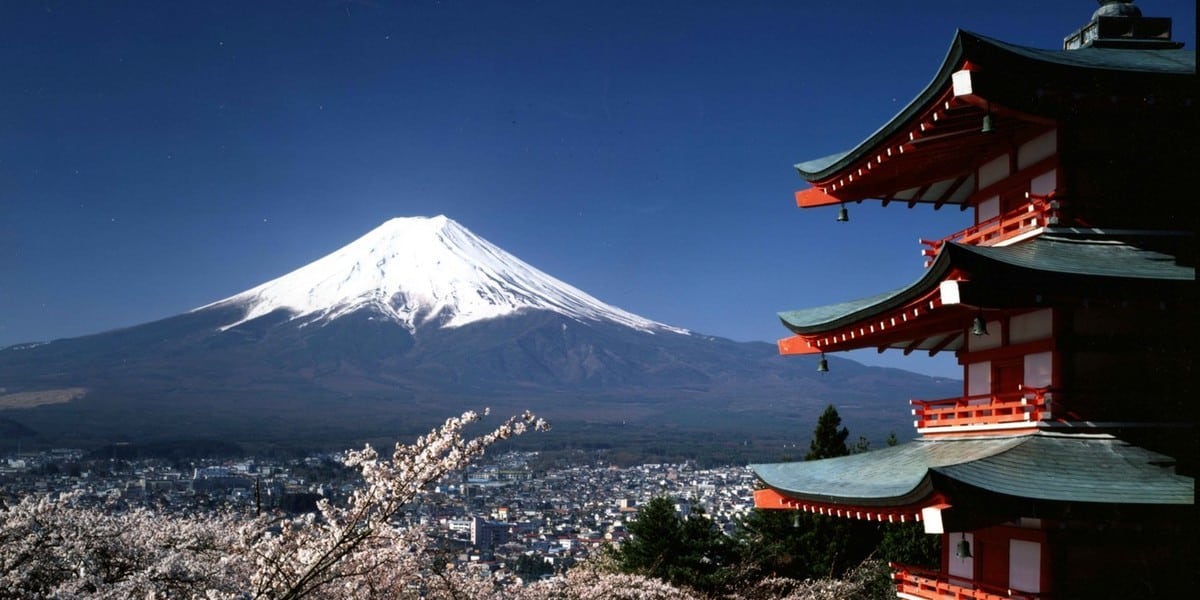 Japón. Japón Vista del Monte Fuji desde un zona de templos, uno de los cuales se puede ver parcialmente a la derecha, y unas ramas de cerezos en flor en primer término abajo, tapando las vistas de la ciudad a los pies del monte, en Japón.