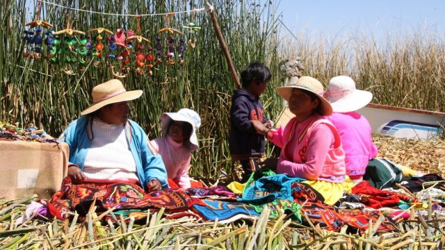 Perú. Mujeres en la isla de los Uros, Puno y Titicaca, sentadas en el suelo y al sol trabajando en diferentes tejidos y bordados, en Perú