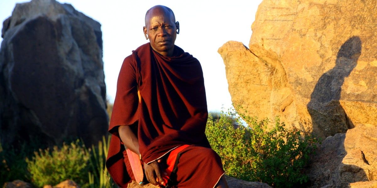 Tanzania. Maasai sentado sobre una roca al atardecer, con su atuendo tradicional, en Tanzania